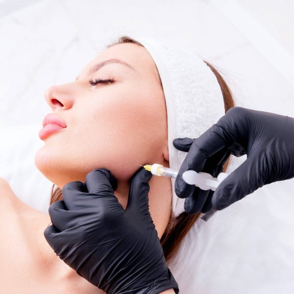 A woman's face getting a Dysport injection procedure on her jawline.